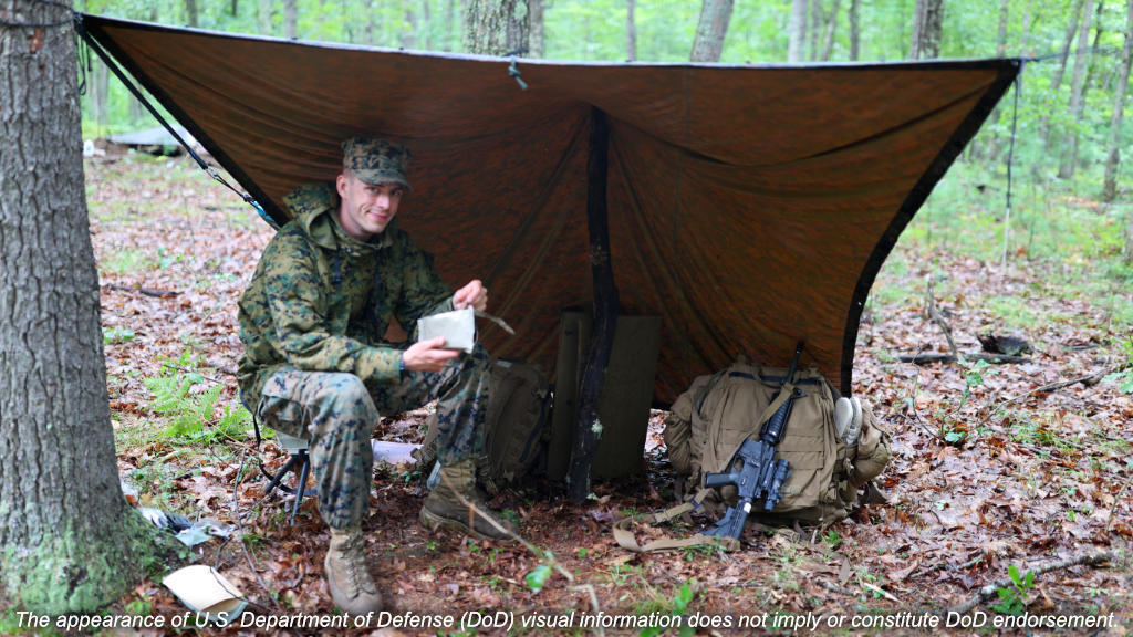Marine under improvised rain fly from military poncho